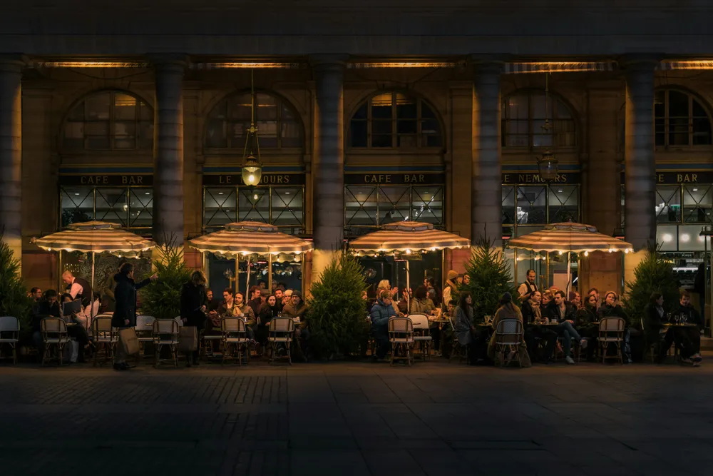 Terrasse animée du restaurant en soirée, tables sous des lampions et clients attablés